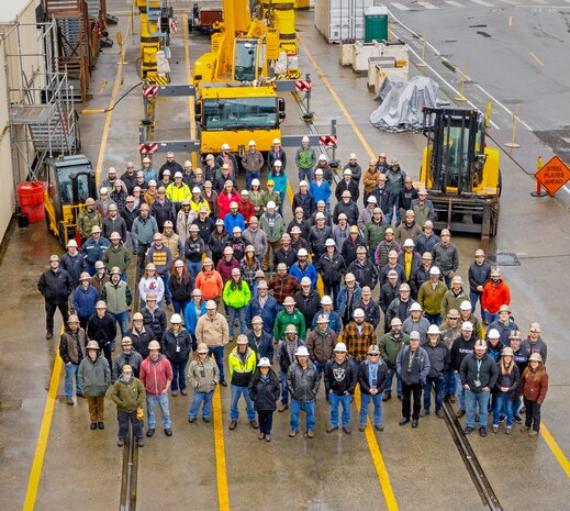 Employees with Code 730, Crane Maintenance, pose for a group portrait Dec. 14, 2023, along the crane maintenance repair tracks outside Building 455 at Puget Sound Naval Shipyard and Intermediate Maintenance Facility in Bremerton. (U.S Navy photo by Wendy Hallmark)