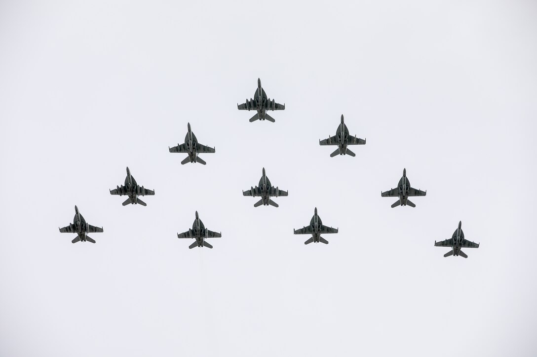 Military aircraft fly in formation against an overcast sky.