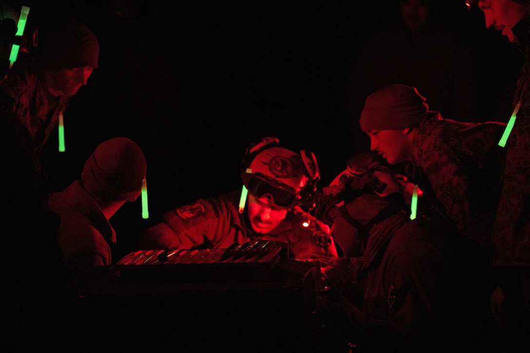 Uniformed Marines work at night, illuminated by red light and green glow sticks in their caps and/or hands.