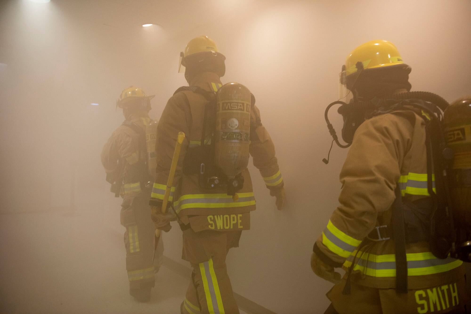 Fire fighters walk through a smokey hallway.