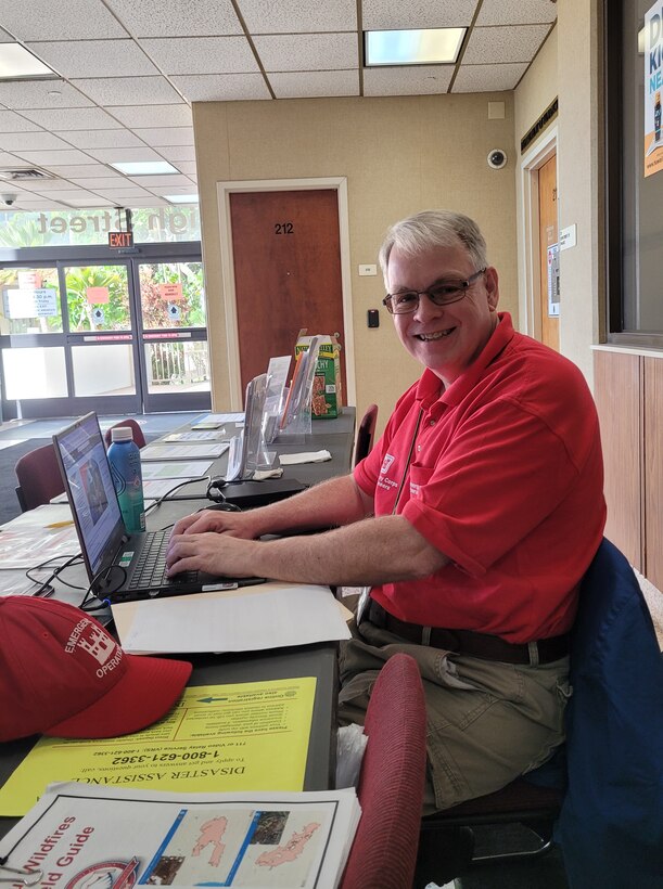 A man in a red shirt sitting at a computer.