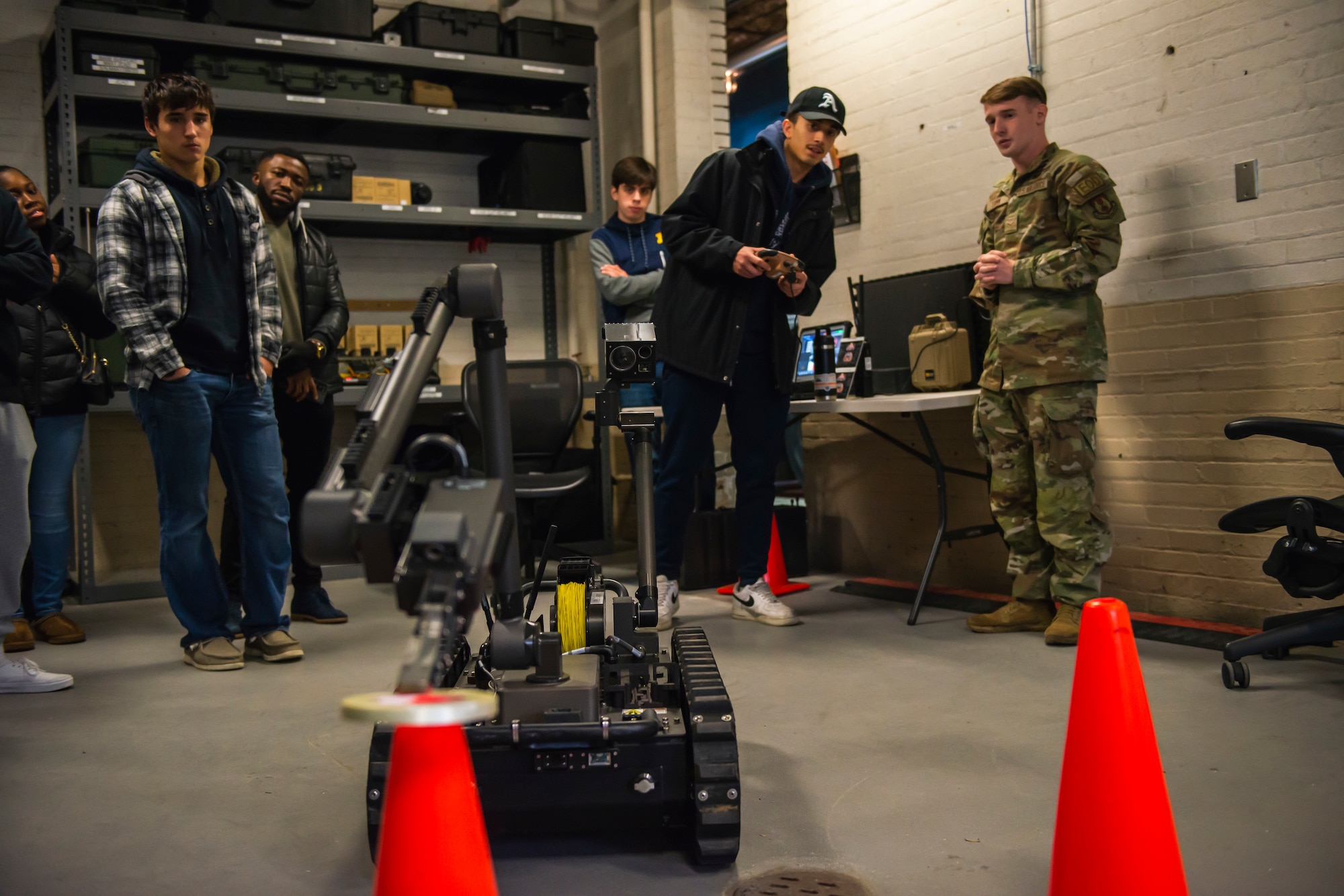 Young man controls a robot with a remote that is lifting a ring off of a cone.