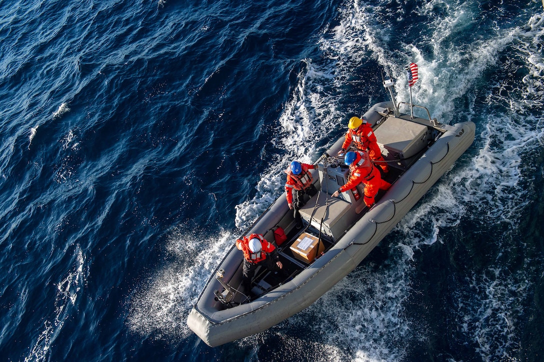 Sailors stand in a rigid hull inflatable boat in open water.