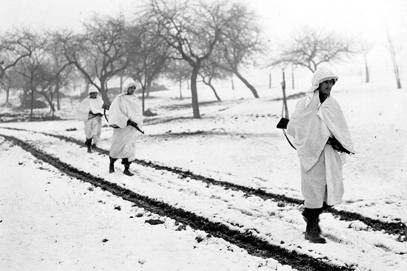 People in white bed sheets walk through snow to blend in.