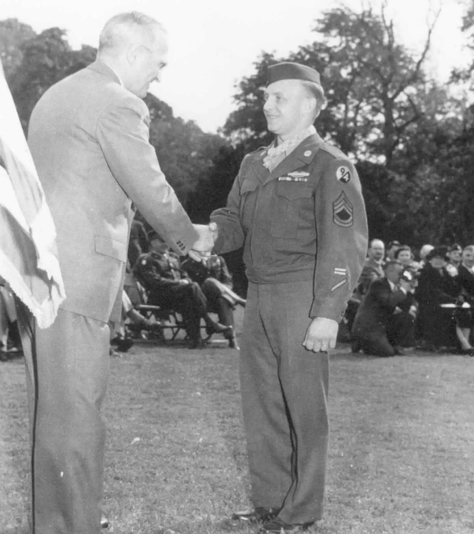 A person in a business suit shakes hands with a soldier.