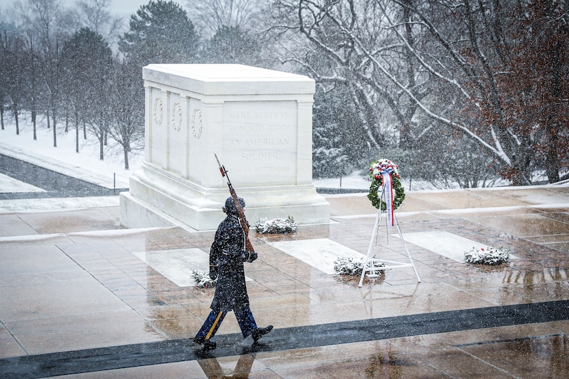 A soldier in a formal uniform carries his rifle as he marches in the snow.