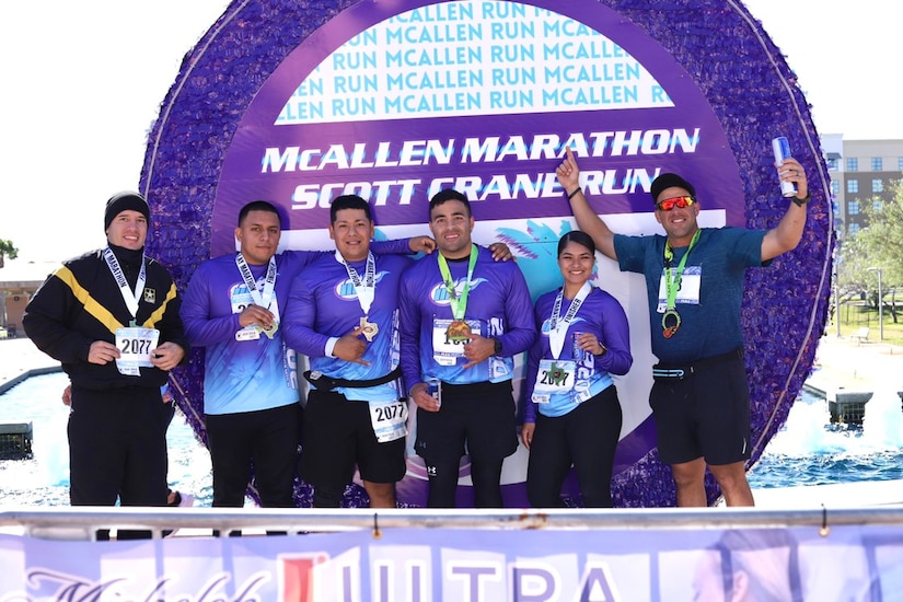 Soldier in pt uniform poses with 5 other athletes in matching shirts at a marathon photo opportunity