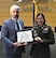 Female Army Soldier in a dress uniform poses with a man in a suit. The Soldier is presenting a plaque for the PaYS program patnership signing ceremony