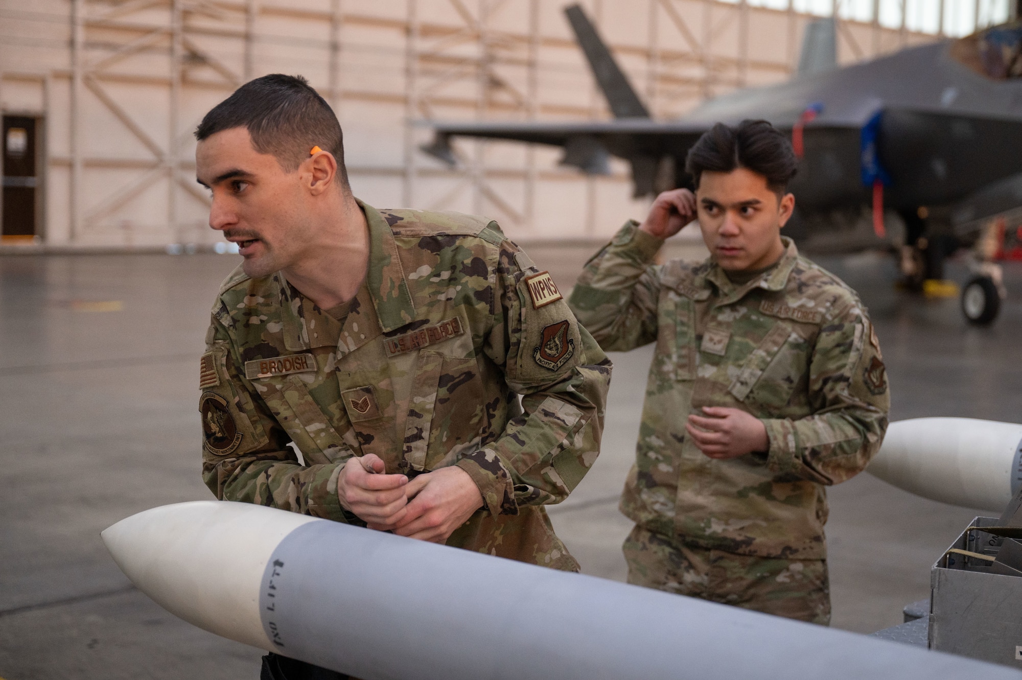 U.S. Air Force Staff Sgt. Trent Brodish (left), 18th Aircraft Maintenance Unit load crew team chief, and Senior Airman Elee Cruz, 18th AMU load crew apprentice, prepare to load a piece of armament during a load competition on Eielson Air Force Base, Alaska, Jan. 11, 2024.
