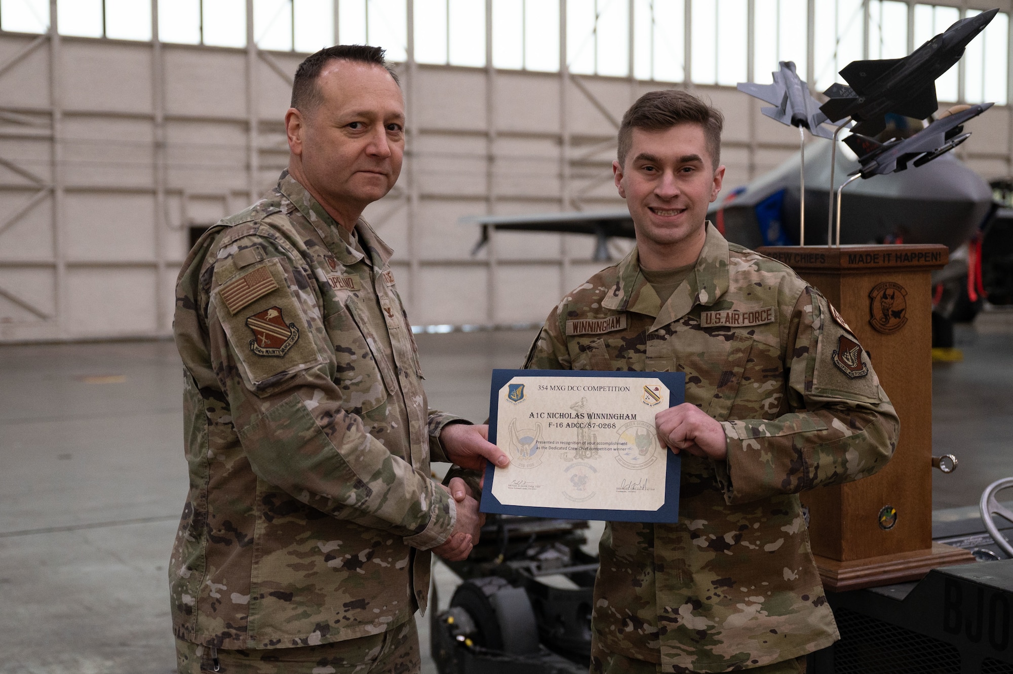 U.S. Air Force Col. Jerrymar Copeland (left), 354th Maintenance Group commander, hands a Dedicated Crew Chief award certificate to Airman 1st Class Nicholas Winningham, 18th Aircraft Maintenance Unit assistant dedicated crew chief, on Eielson Air Force Base, Alaska, Jan. 11, 2024.