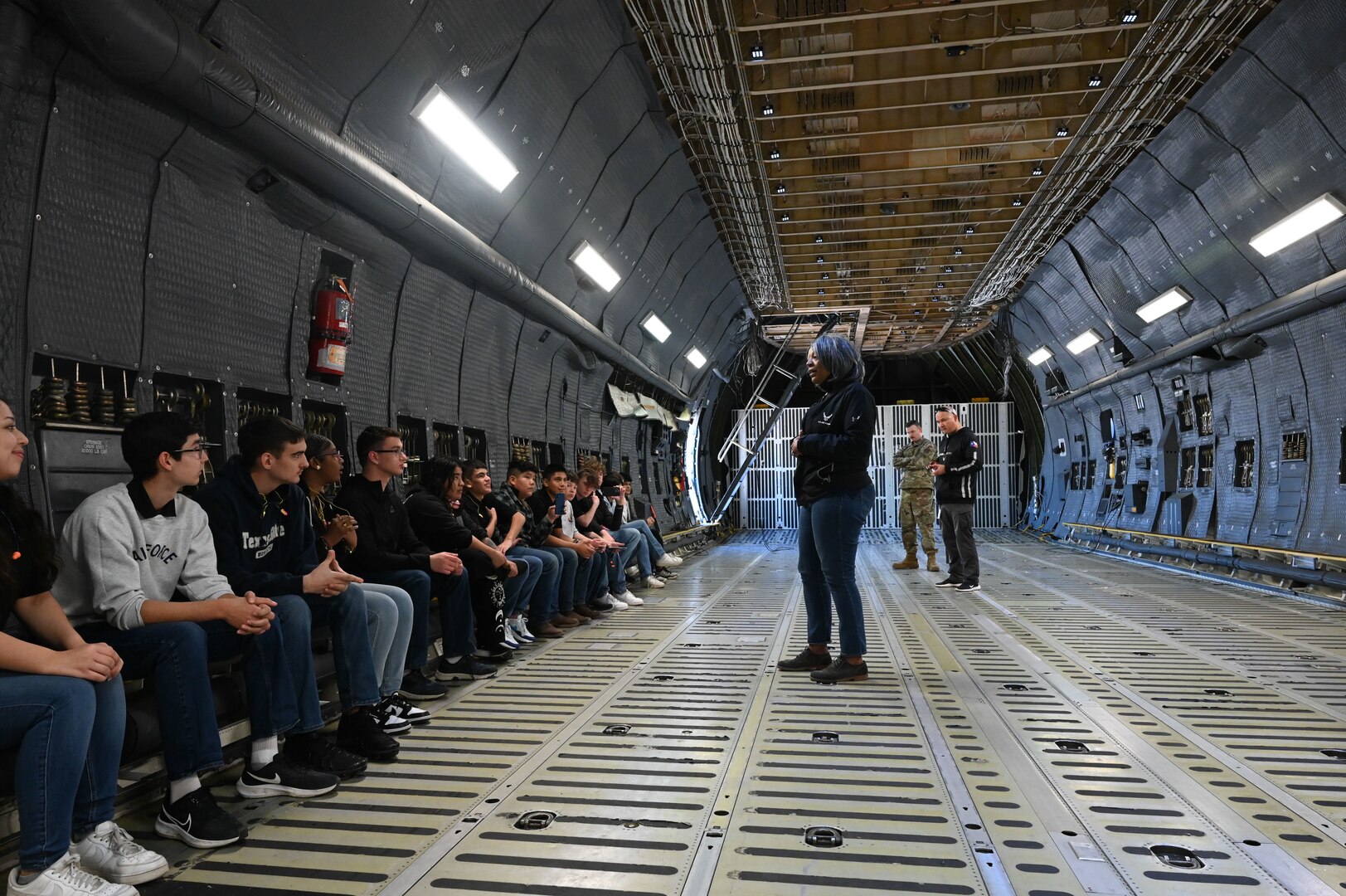 Ms. Minnie Jones, 433rd Airlift Wing Public Affairs operations chief, center, briefs Thomas C. Clark High School Junior Reserve Officer Training Corps students about the wing’s mission aboard a static C-5M Super Galaxy aircraft at JBSA-Lackland, Texas, Jan, 12, 2024 as part of their installation visit.