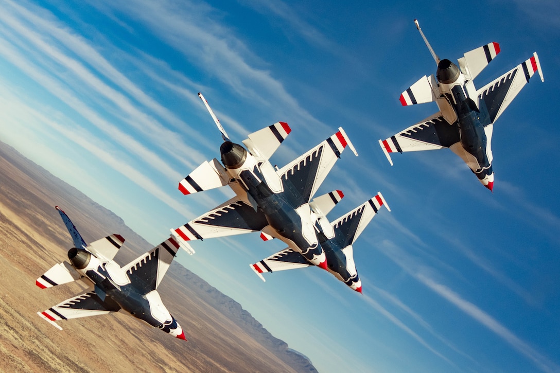 Four military aircraft fly in a diagonally-angled formation over the desert during daylight.