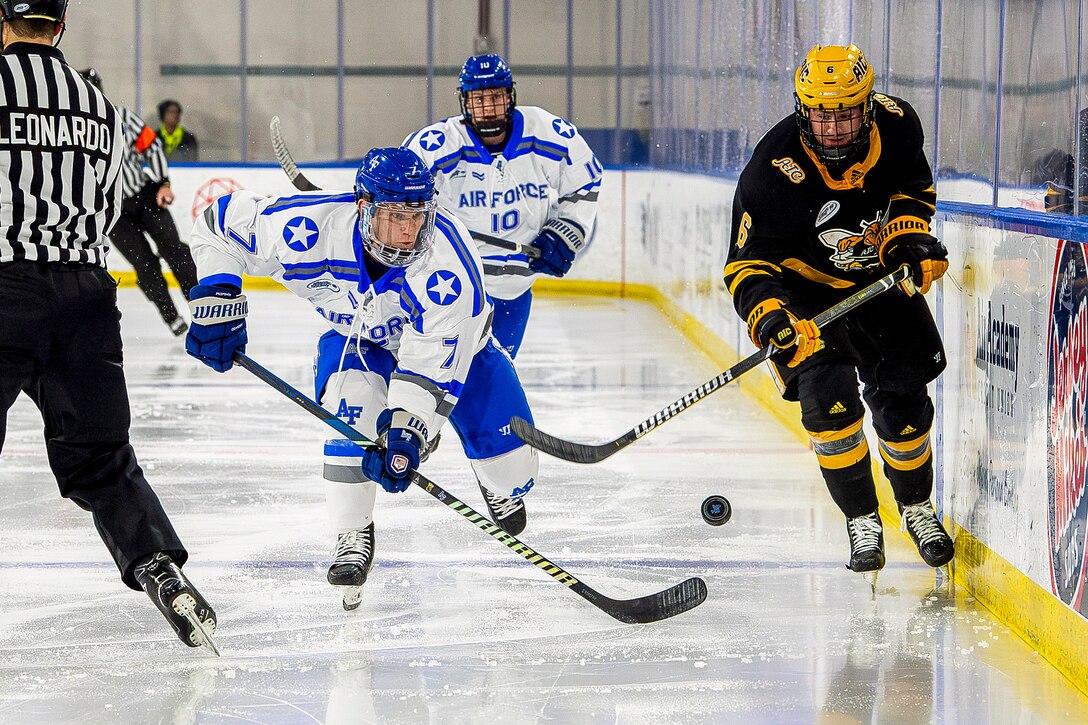 Hockey players skate on ice to get a descending puck as two referees skate on the left.