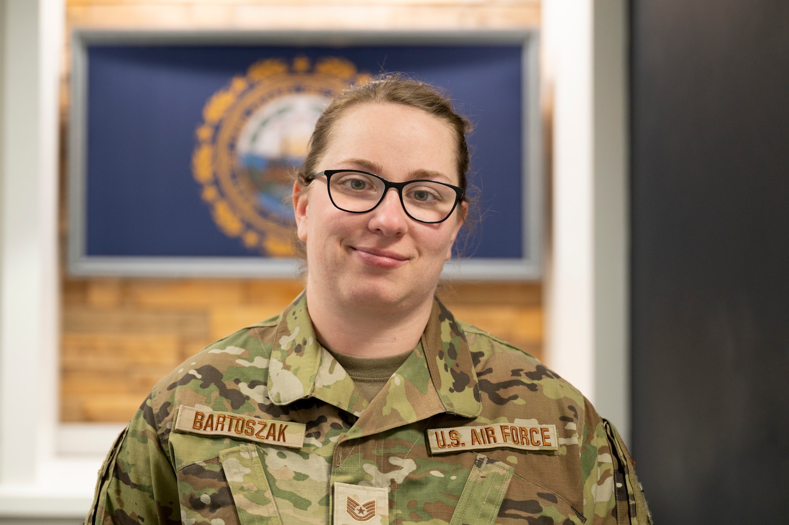 Tech. Sgt. Yvonne Bartoszak, a member of the Traffic Management Office with the 157th Logistics Readiness Squadron, poses in front of the New Hampshire flag Jan. 17, 2024, at Pease Air National Guard Base, New Hampshire. Bartoszak helped an elderly man with dementia in Newington Jan. 3.