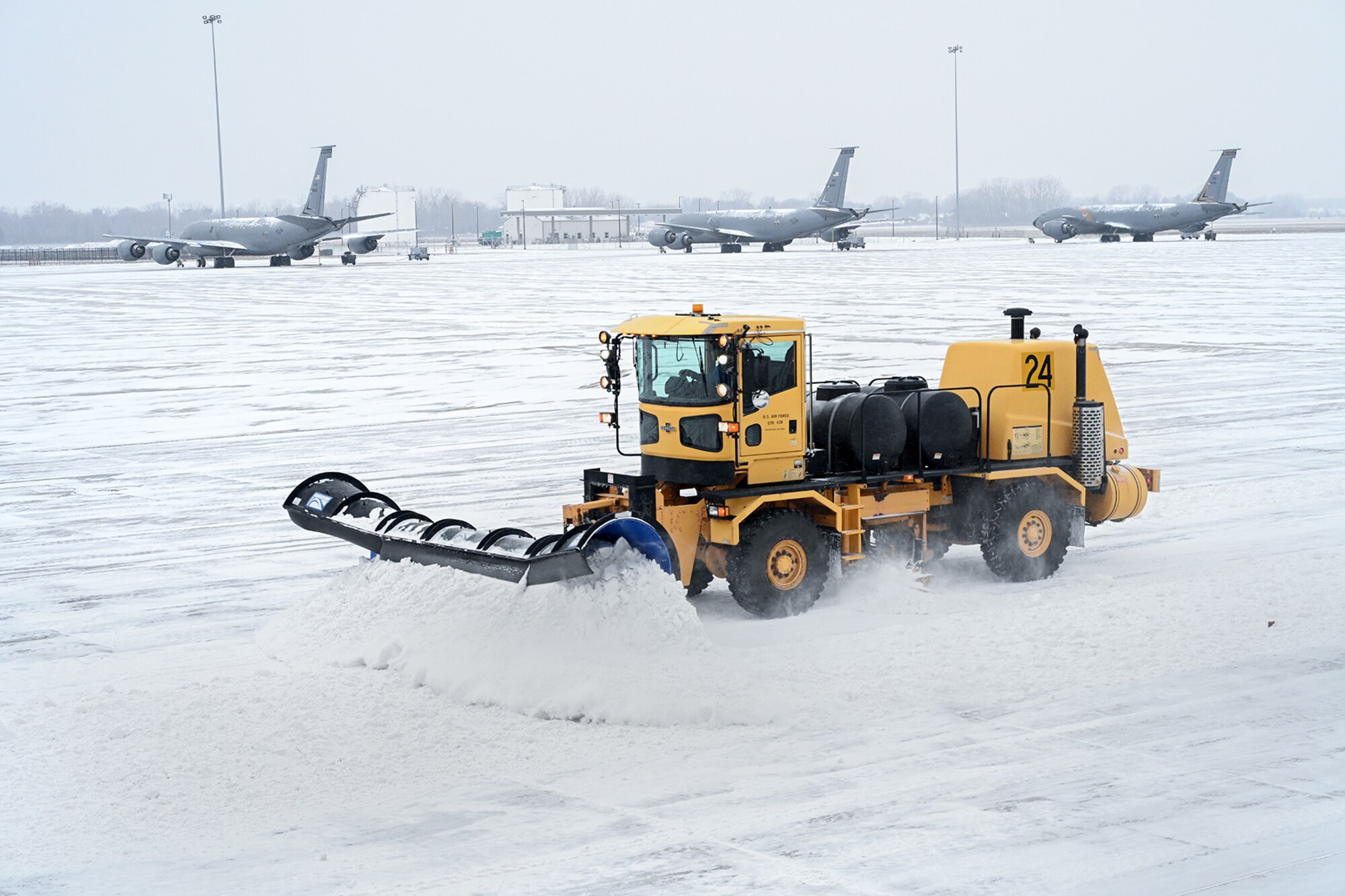Large snow plow on airport flight line with aircraft in the background.