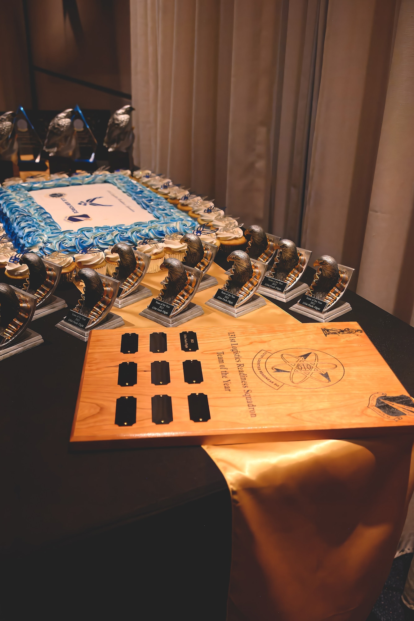 Various award plaques and trophies are displayed on a table along with a cake during an awards ceremony.