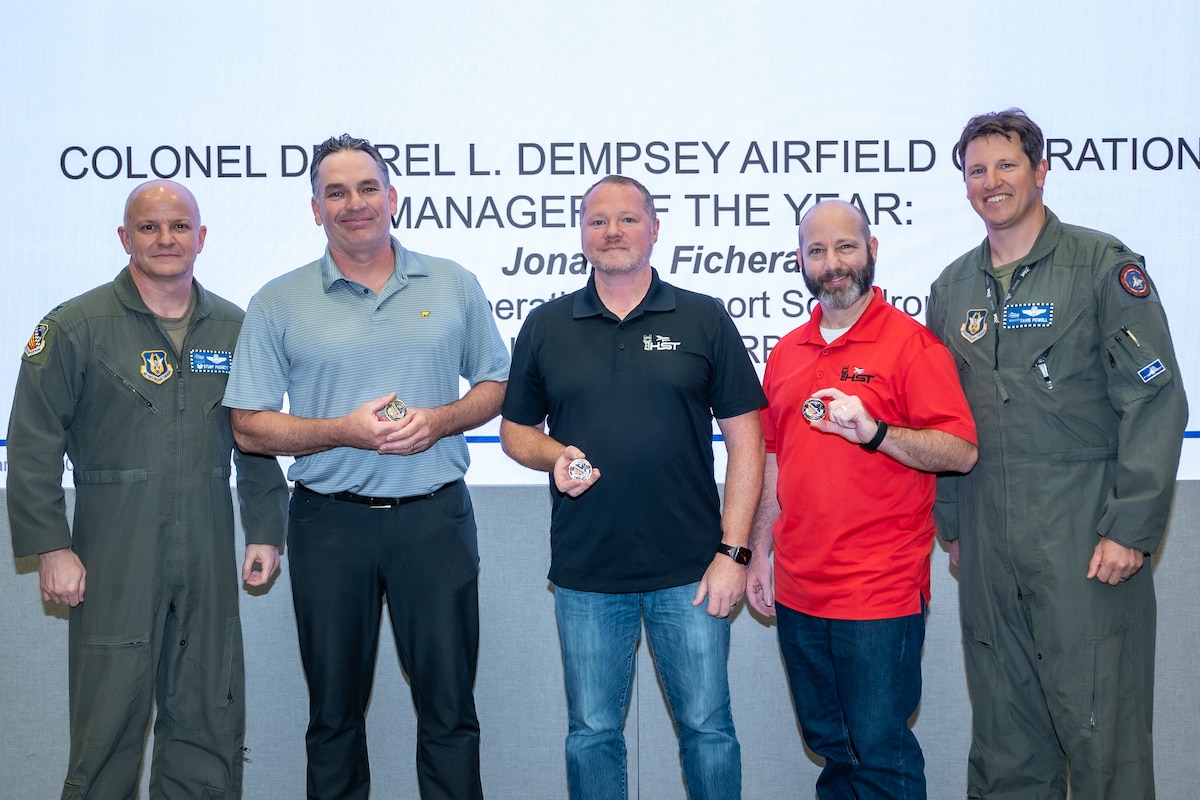 Col. Joshua Padgett, Chris Ziarno, Patrick Archer, Jonan Fichera, and Col. Tavis Powell stand in line at Homestead Air Reserve Base, FL, on Jan. 5, 2024, showcasing a coin awarded for excellence in airfield operations.