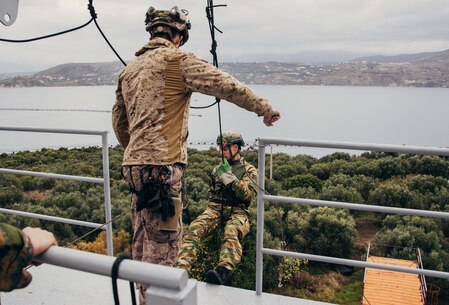A U.S. Marine with the Battalion Landing Team 1/6, 26th Marine Expeditionary Unit (Special Operations Capable) (MEU(SOC)), instructs Hellenic Marines assigned to the 32nd Hellenic Marine Brigade on how to properly rappel down a tower during fast rope and rope suspension training at Naval Support Activity Souda Bay, on the island of Crete, Greece, Dec. 18, 2023. U.S. Marines and Sailors of the 26th Marine Expeditionary Unit (Special Operations Capable), embarked on the ships of the Bataan Amphibious Ready Group, are on a scheduled deployment with elements deployed to the U.S. 5th Fleet and U.S. 6th Fleet areas of operation to increase maritime security and stability, and to defend U.S., Allied, and Partner interests. (U.S. Marine Corps photo by Cpl. Aziza Kamuhanda)