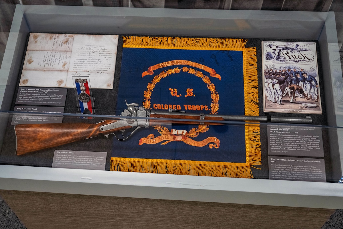 A shadow box display contains the 26th United States Colored Infantry Regiment Banner - 1864,  a firearm and other gear.