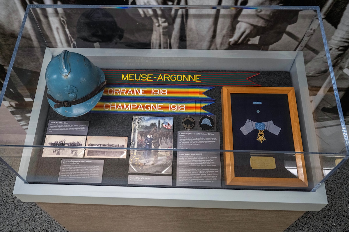 An display case shows artifacts including a French M15 Adrian Helmet, Stereograph cards, recruiting posters, 92nd and 93rd Infantry Division Patches and Freddie Stowers’ Medal of Honor.