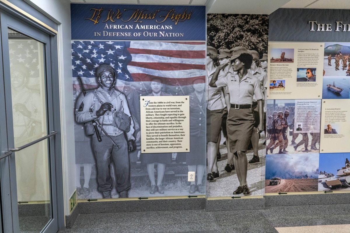 A graphic of text and photos depicting African Americans who served in the military is shown on a wall next to a glass door.