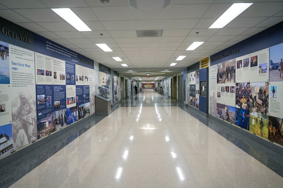 A long view down a corridor with both walls lined with displays of text, images and cases containing artifacts.
