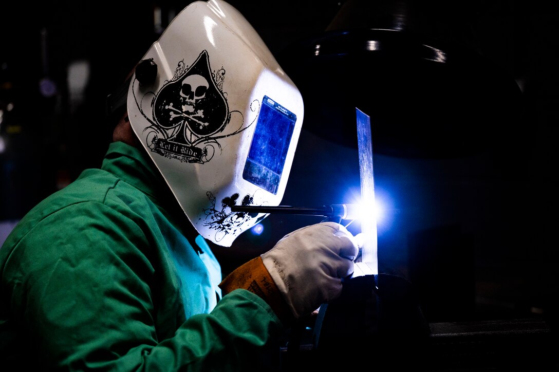 An airman in a protective suit and helmet practices welding.