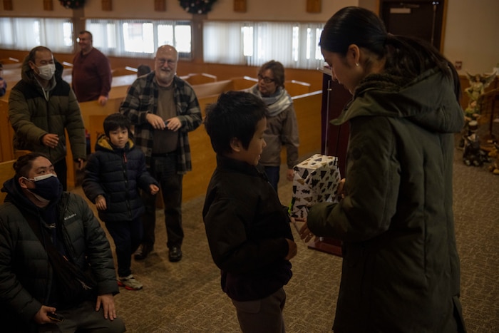 An Angel Tree Gift volunteer hands a present to a child during an Orphanage Angel Tree Gifts and Pool Party at Misawa Air Base, Japan, Dec. 16, 2023.