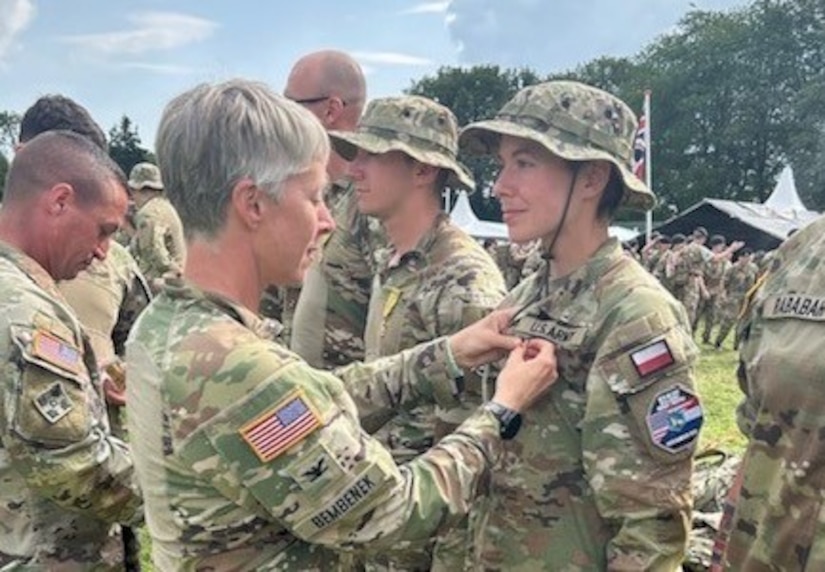woman wearing an army uniform pins a ribbon on the uniform of another women soldier wearing an army uniform.
