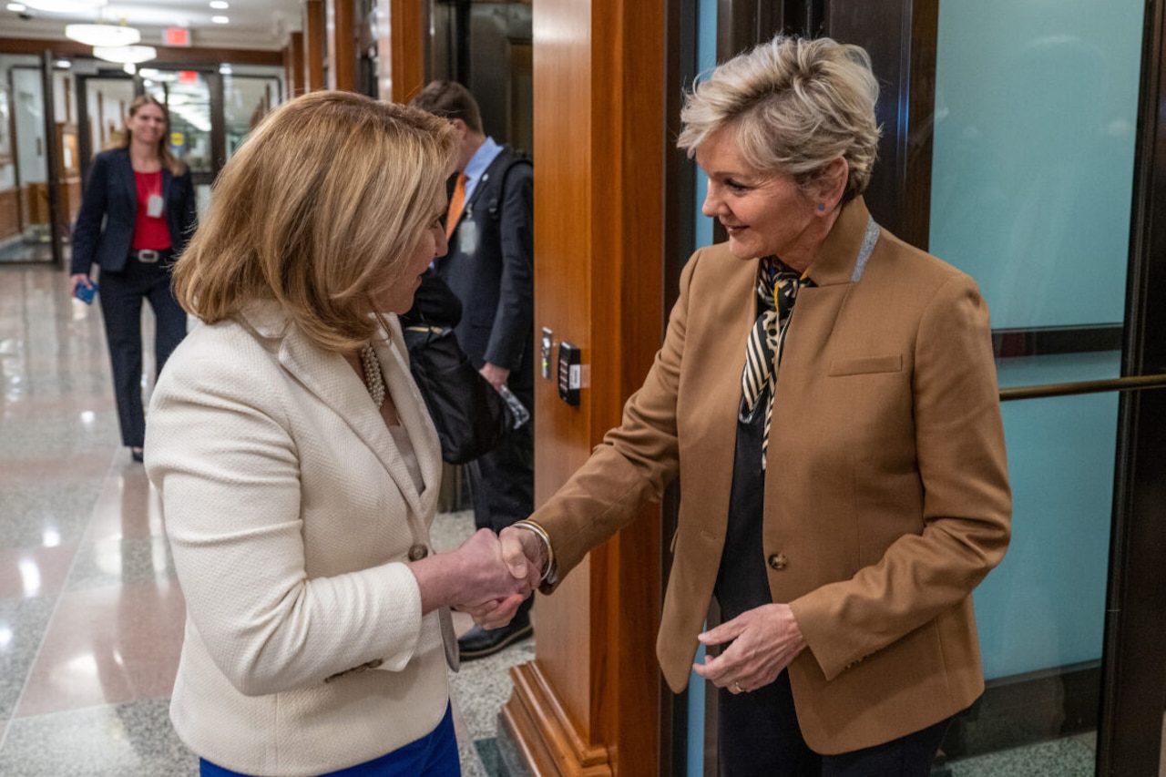 Two women wearing civilian clothes shake hands.