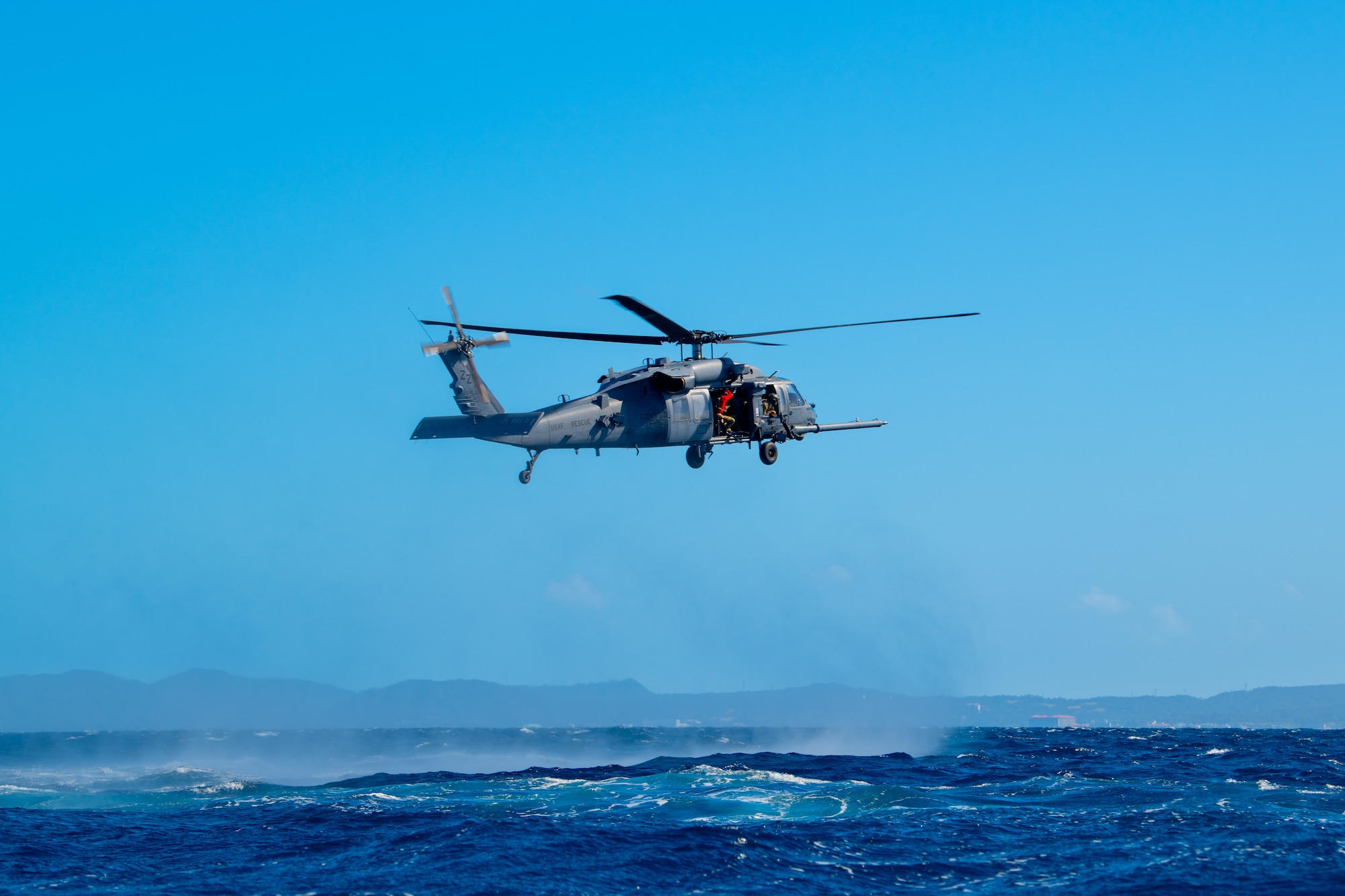 An HH-60G Pave Hawk hovers above the ocean.