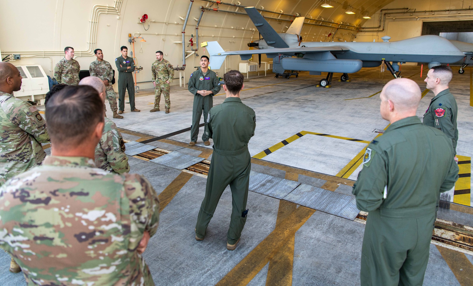 A group listens to a service member discuss the capabilities of the MQ9 behind him.