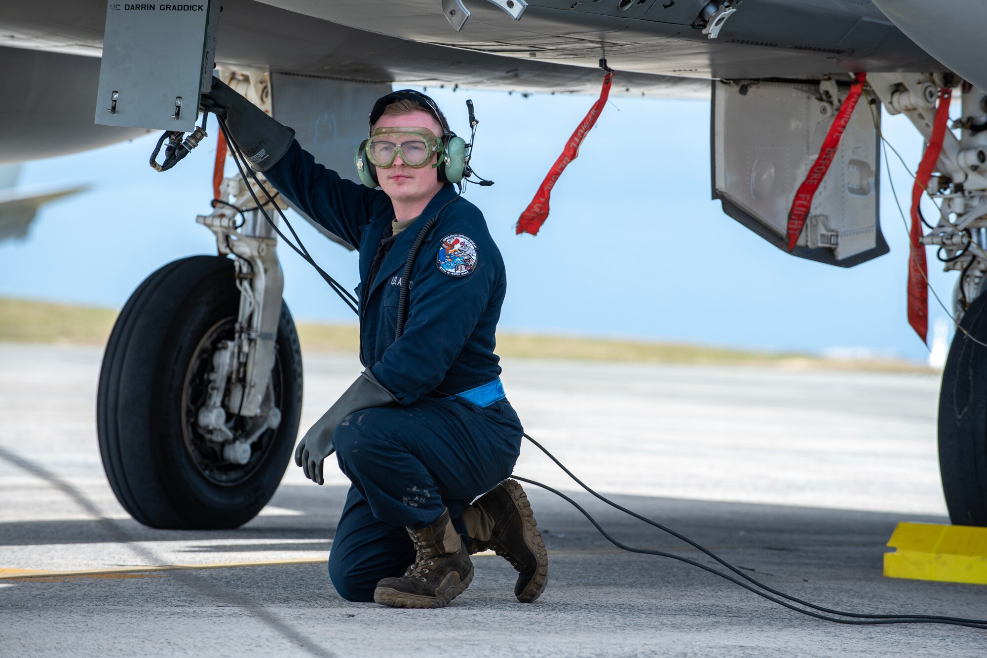 airmen kneels underneath a plane hooking up communication lines