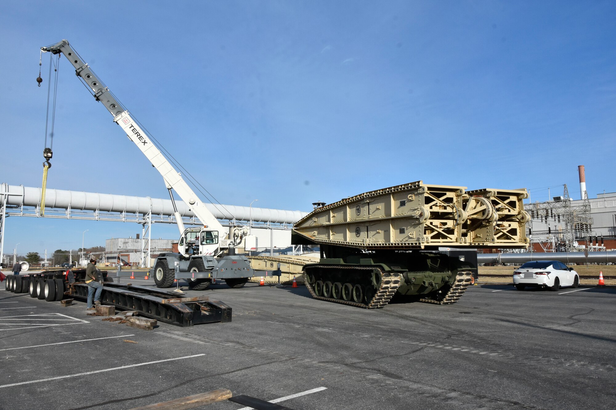 The crane and rigging crew at Arnold Air Force Base provide crane support Nov. 30, 2023, support to off-load a bridge to be used by an Armored Launched Vehicle Bridge. The vehicle was commercially delivered to Arnold AFB, Tenn., from Fort Campbell, Ky., that same day, and the crew stayed late to ensure mission success. AVLBs carry a deployable bridge and are designed to allow tanks, infantry fighting vehicles and other tactical vehicles to cross small rivers, gaps and other terrain obstacles on the battlefield. It was needed to move a large crane across an Arnold alleyway where the axle load limit was less than the weight of the crane. The bridge component of the AVLB was emplaced on Jan. 6, 2024, to allow the crane entrance into the work area. The AVLB was operated by a Guardsman with the 190th Engineer Company of the Tennessee National Guard, while Guardsmen from the 194th Engineer Brigade directed and guided the operation. (U.S. Air Force photo by Bradley Hicks) (This image was altered by obscuring a vehicle license plate)