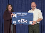 Two business professionals stand in front of a blue curtain holding a card with CFC and DCAA branding along with Goal $33,000