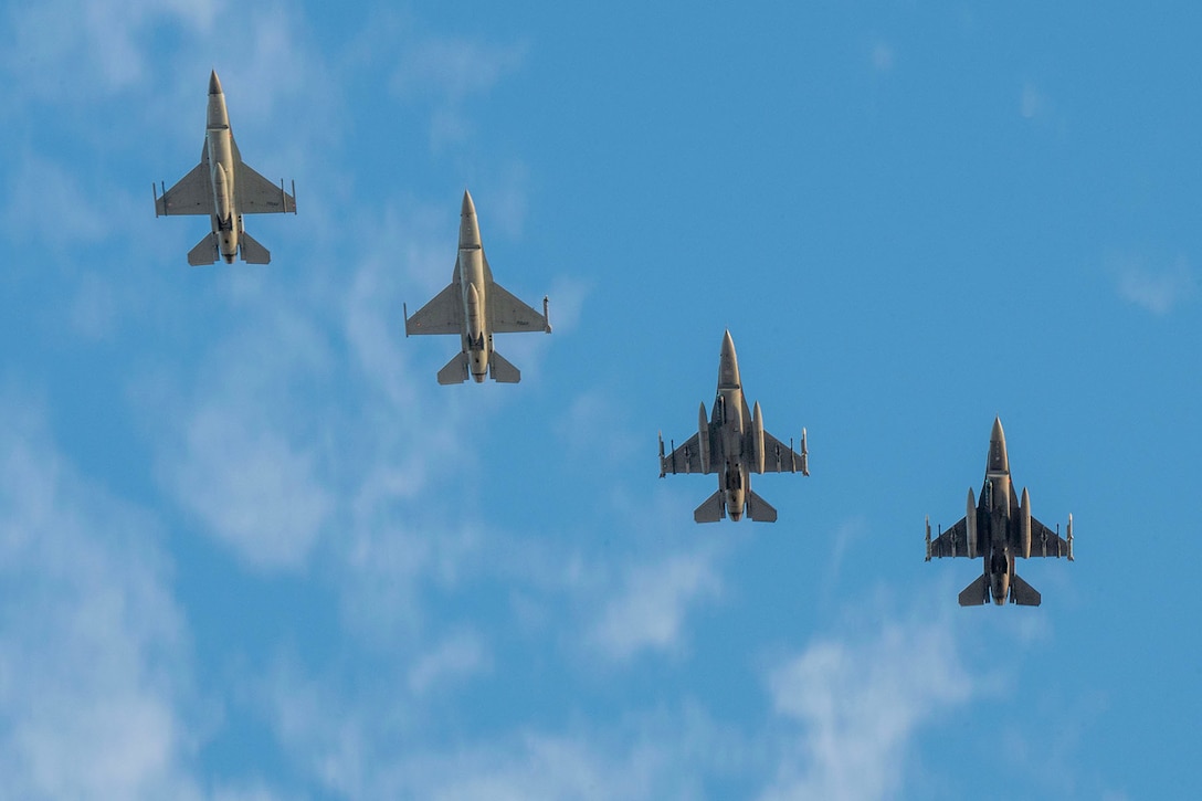Four military aircraft fly in formation during daylight. The photo is from beneath the aircraft.