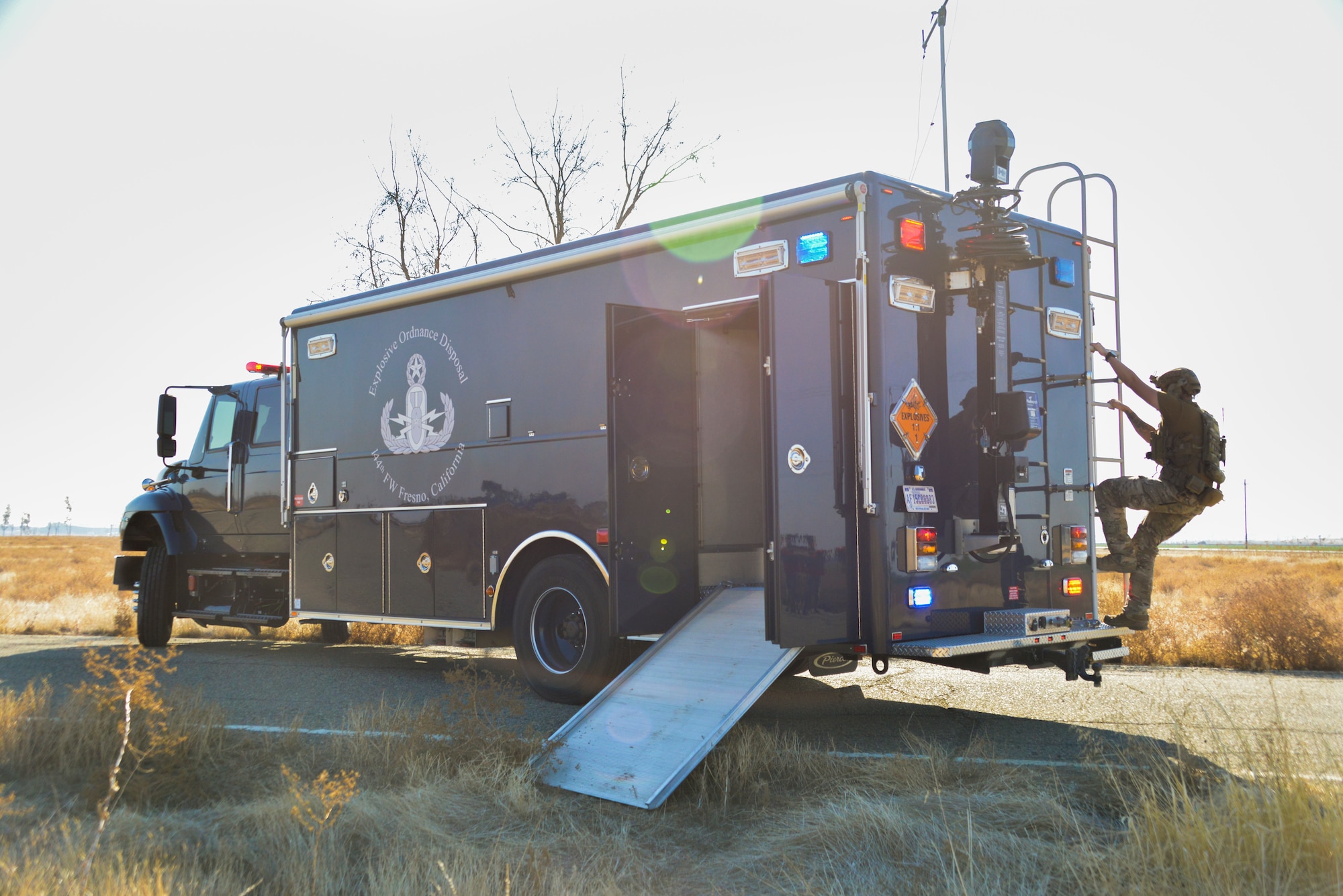 An Airman climbs the ladder on the rear of a blue emergency response vehicle.
