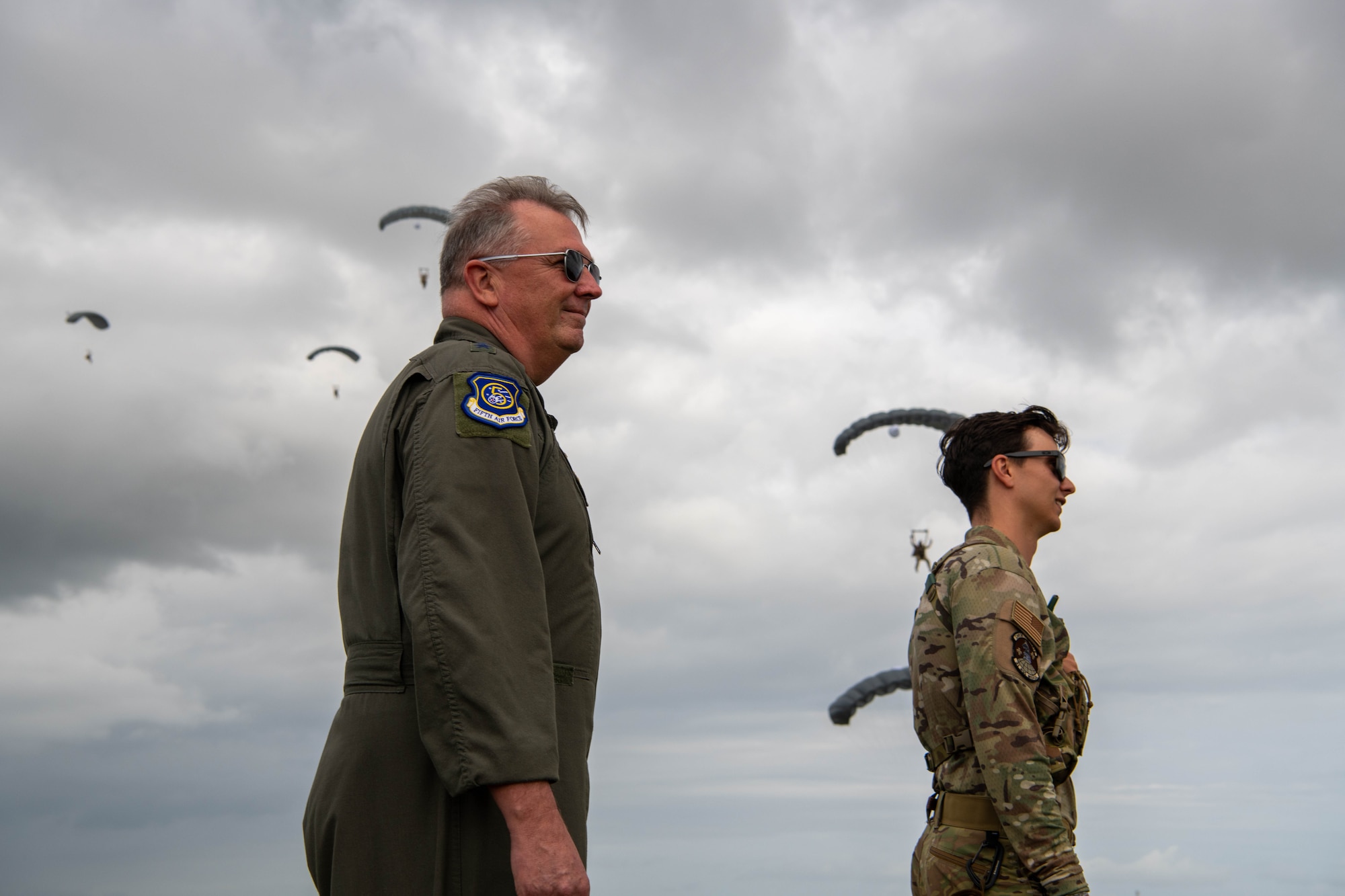 5th Air Force leadership watches pararescuemen parachute in the sky.
