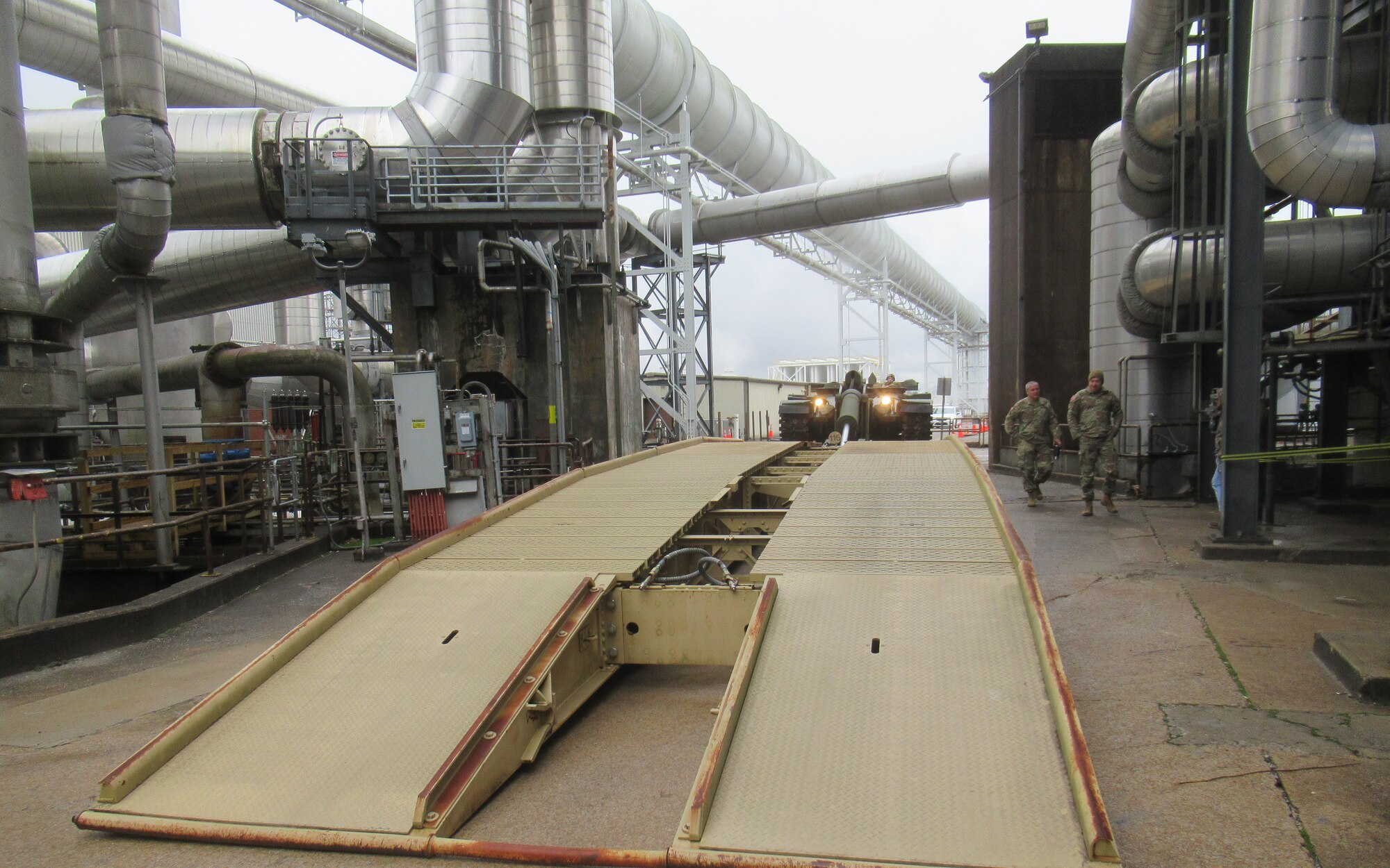 The bridge component of an Armored Vehicle Launched Bridge is emplaced Jan. 6, 2024, over the second entryway crossing into a work area at Arnold Air Force Base, Tenn. AVLBs carry a deployable bridge and are designed to allow tanks, infantry fighting vehicles and other tactical vehicles to cross small rivers, gaps and other terrain obstacles on the battlefield. The AVLB was commercially delivered to Arnold from Fort Campbell, Ky., on Nov. 30, 2023, and was needed to move a large crane across an Arnold alleyway where the axle load limit was less than the weight of the crane. The AVLB was operated by a Guardsman with the 190th Engineer Company of the Tennessee National Guard, while Guardsmen from the 194th Engineer Brigade directed and guided the operation. (U.S. Air Force photo)