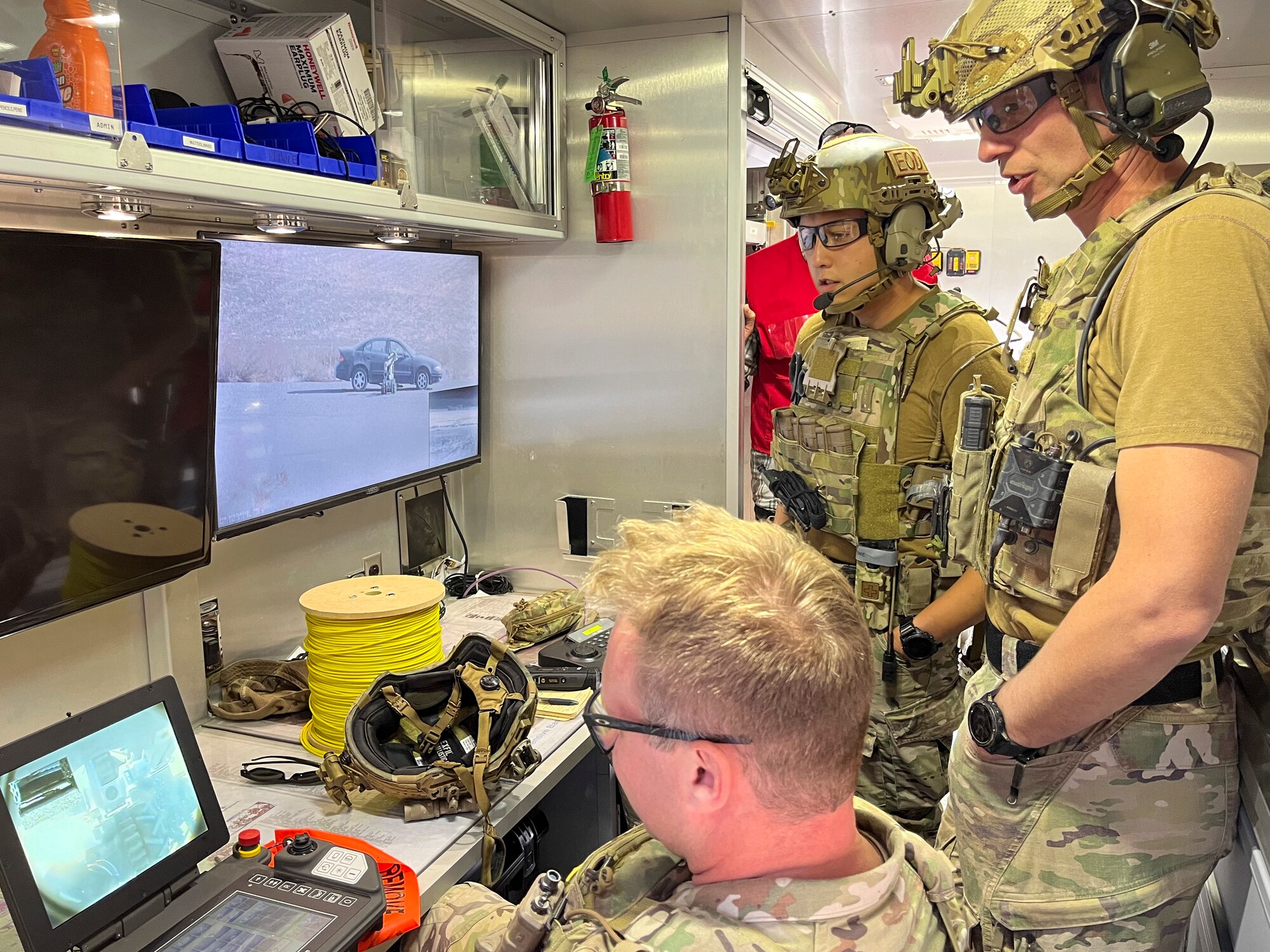 Three Airmen look at two screens to control a robot remotely.