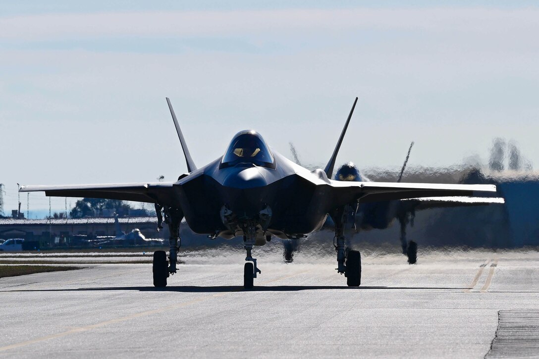 Two fighter jets line up behind each other on a runway.