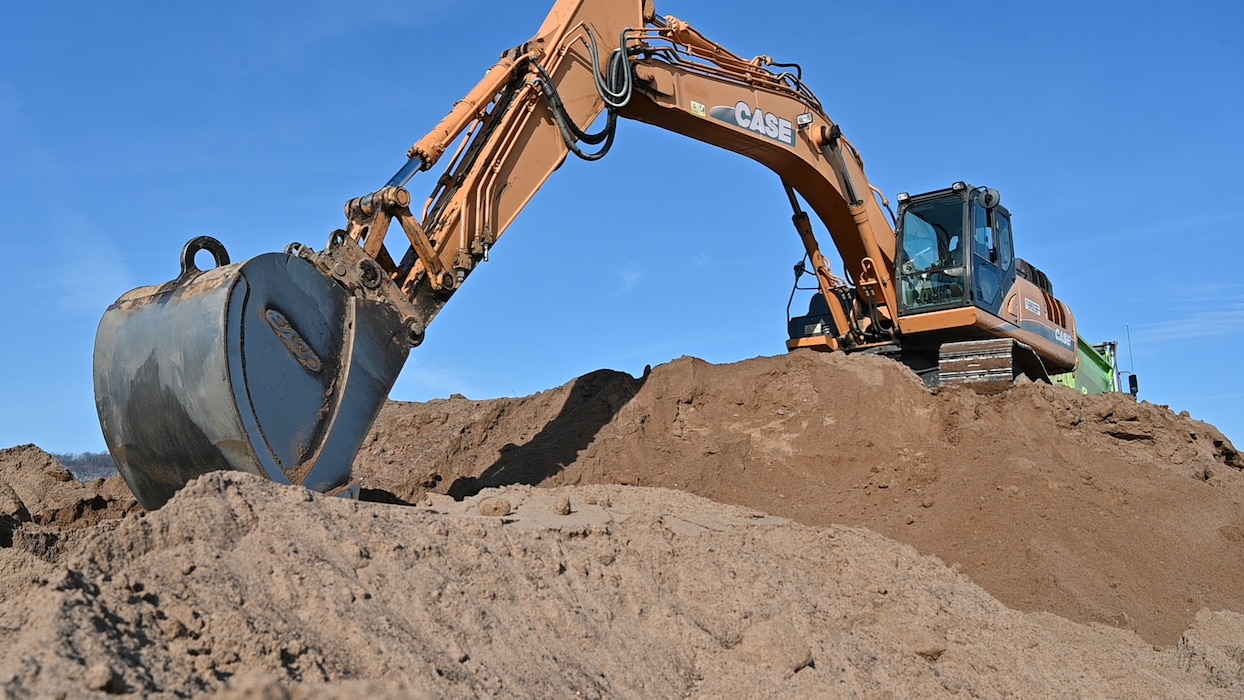 An excavator scoops sand into a bucket atop a larger pile of sand.