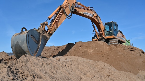 construction equipment scoops sand into a bucket atop a larger pile of sand.