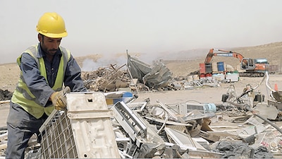 Man wearing a reflective vest and hard hat in a field of what looks to be metal moves a boxy looking item.