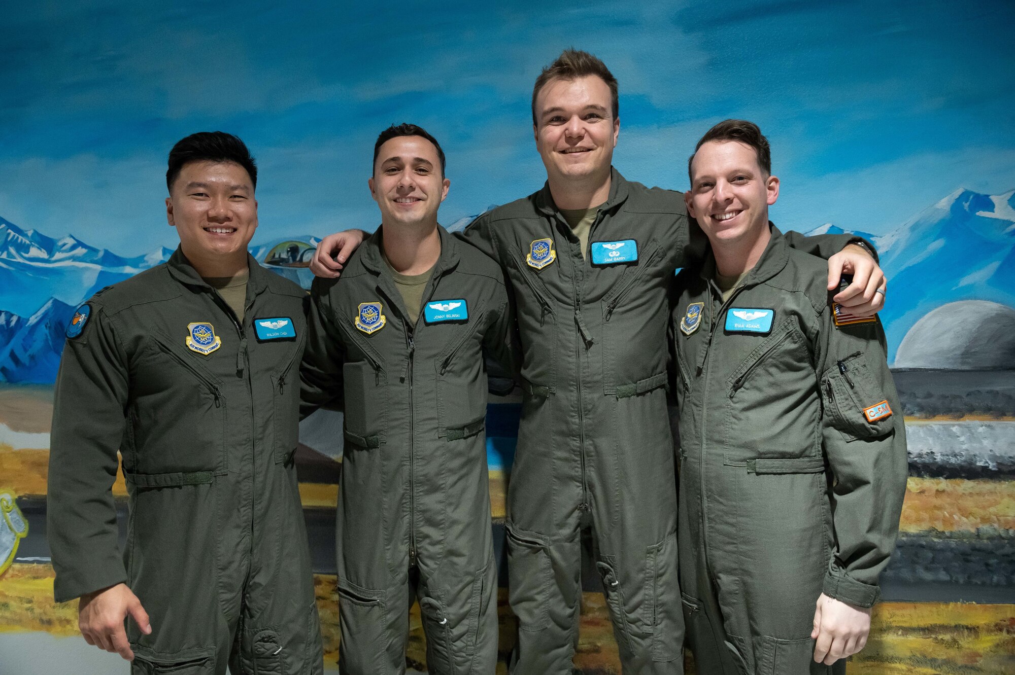 Four men pose for a photo wearing flight suits