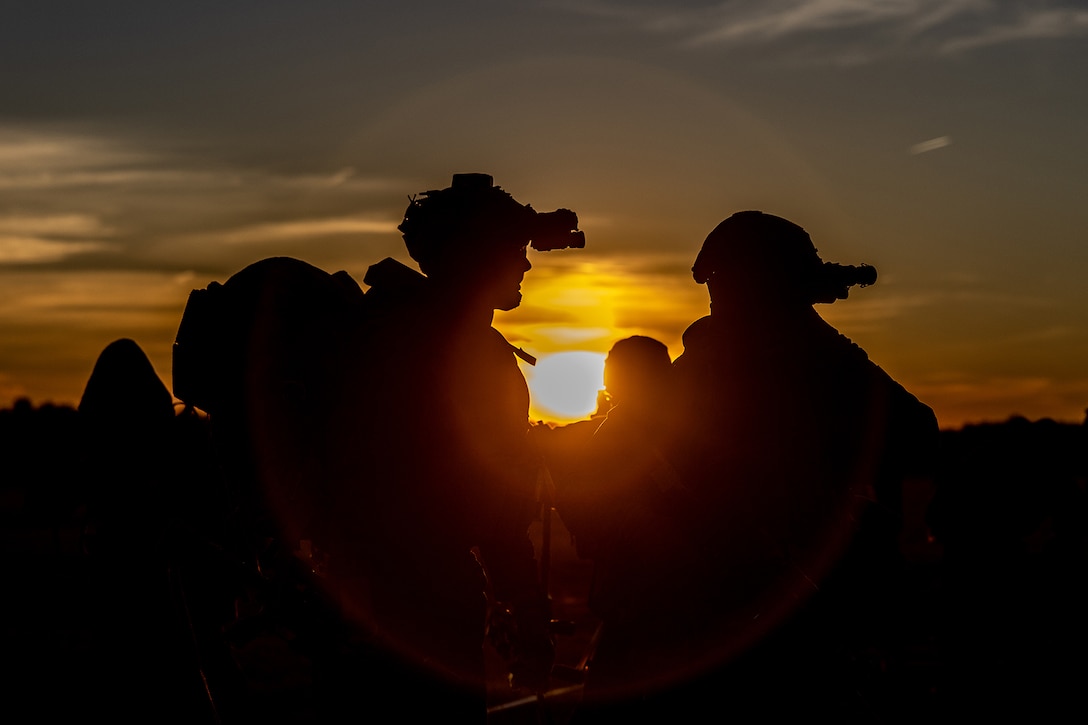 A group of Marines are shown in silhouette, standing outdoors, illuminated by a low sun.