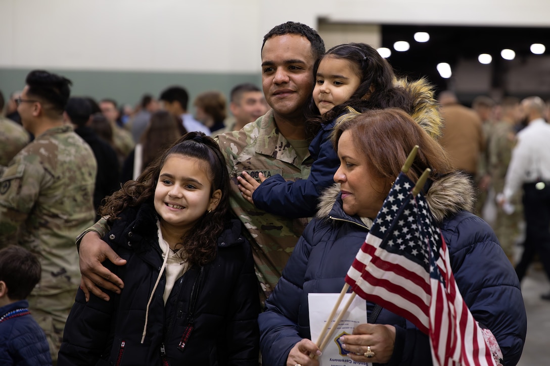 A soldier holds a child while standing with two other people during a pre-deployment send-off.