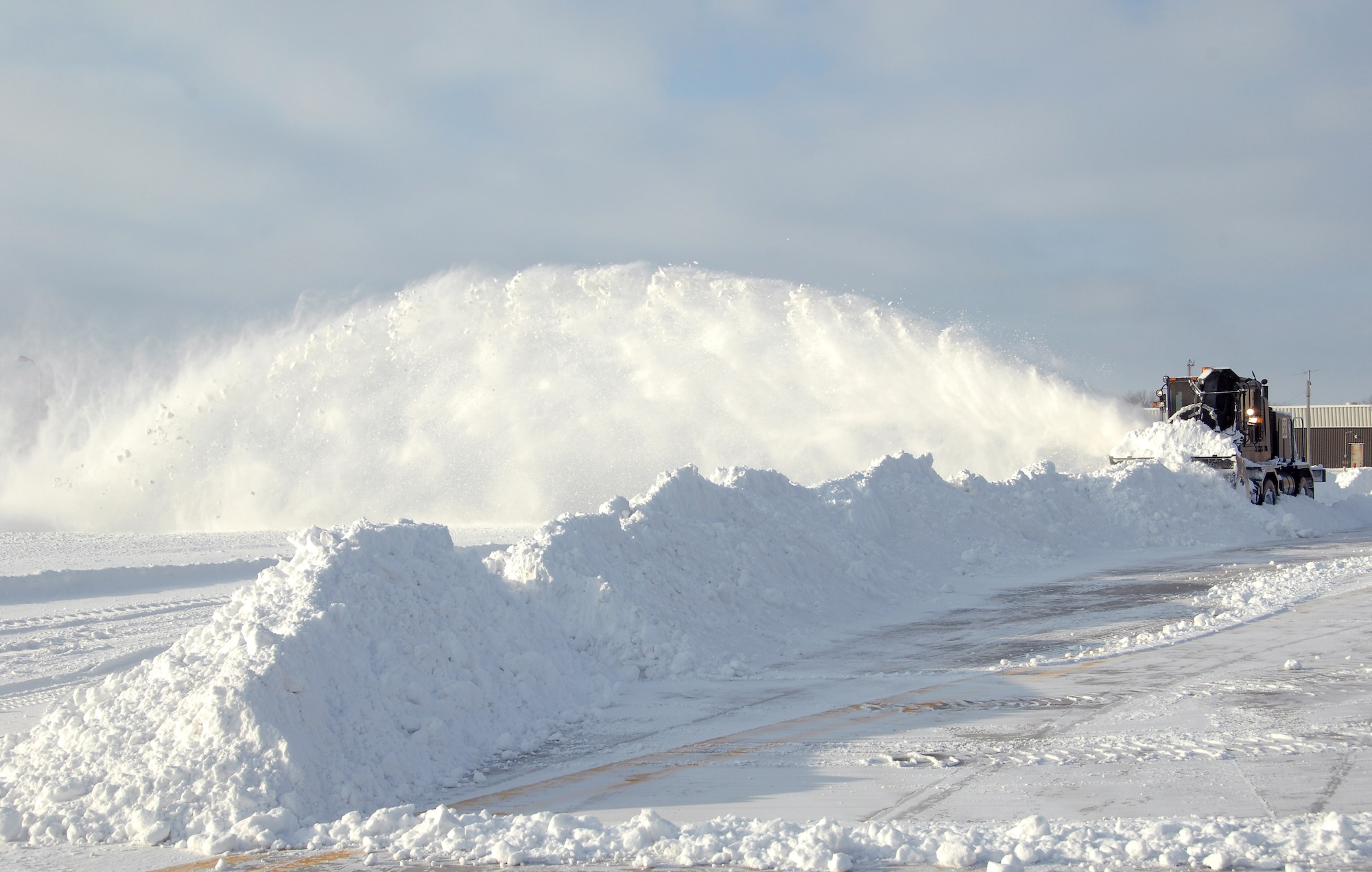 a huge snow machine blows a fan of snow on an airfield