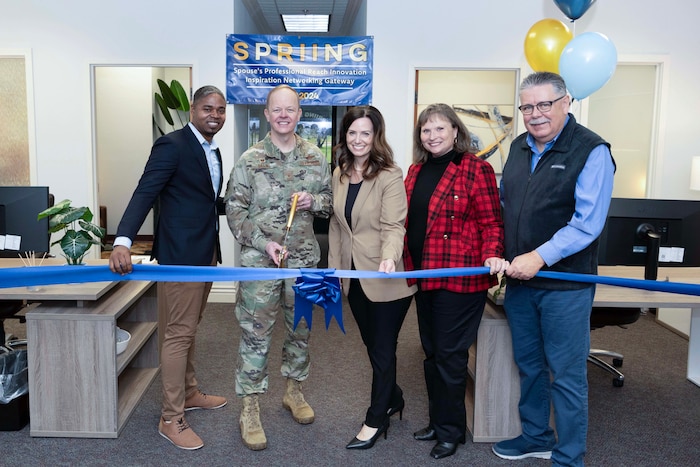 An Airman and civilian leaders pose in front of a ribbon for a photo.