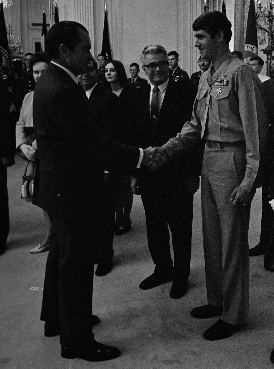 A man in a business suit shakes hands with a uniformed service member.